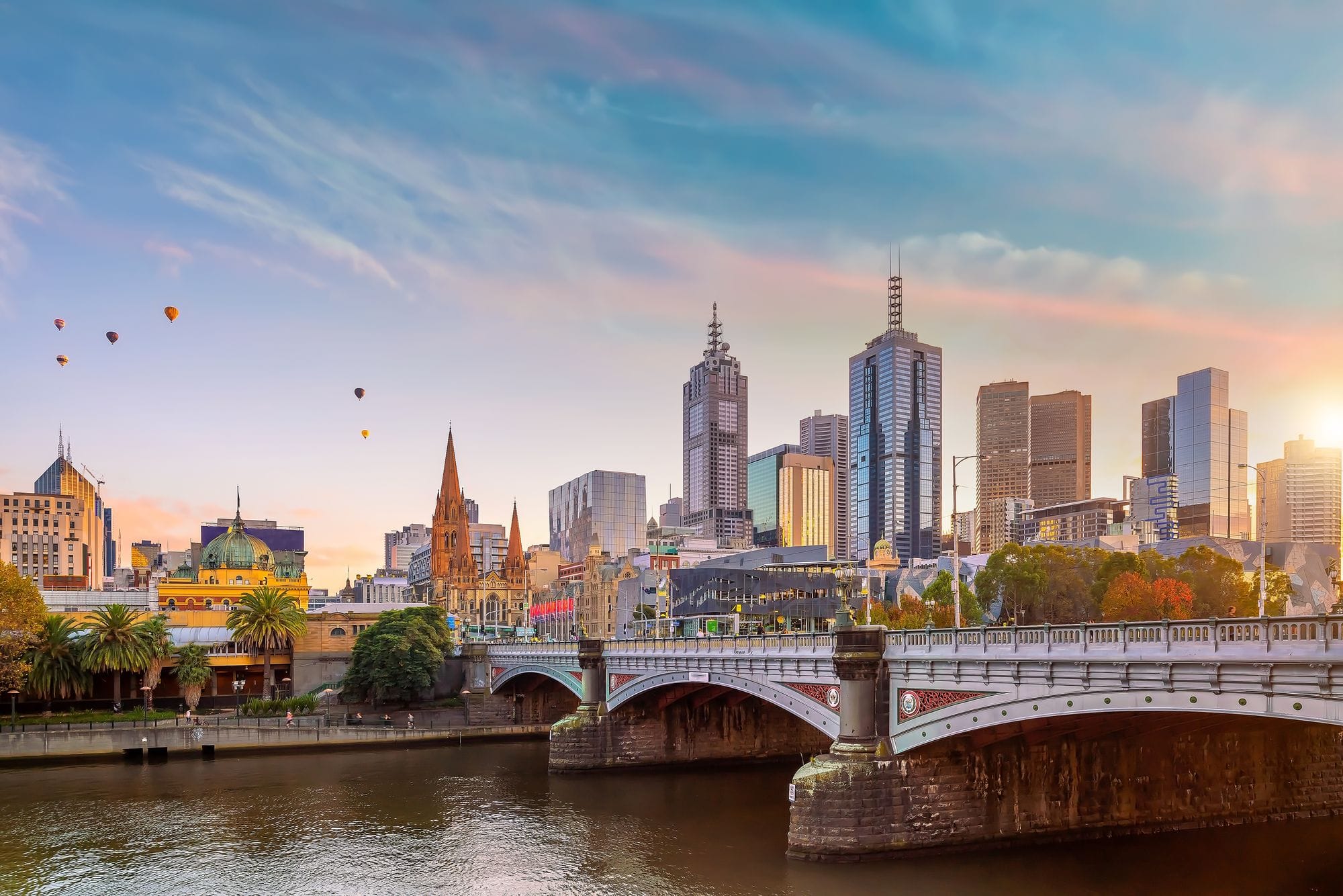 Melbourne cityscape with river, bridge, and skyline at sunset.
