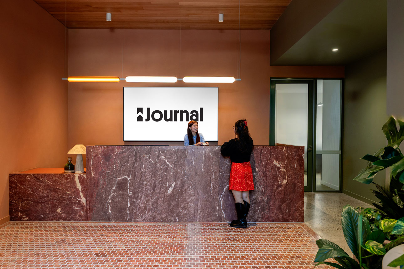 Reception area with two people talking at a marbled front desk.