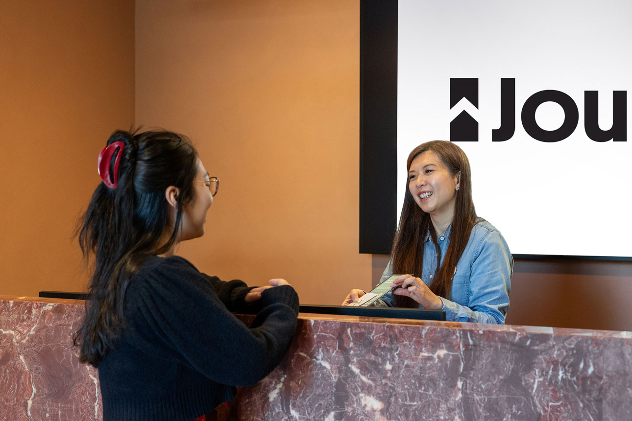 Two people interacting at a reception desk in a modern office setting.