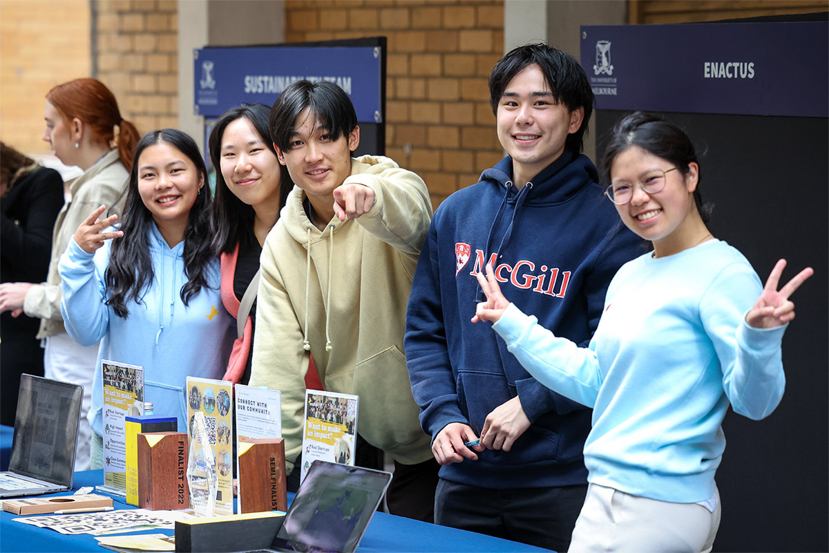 Five students smiling behind a table at a university event.