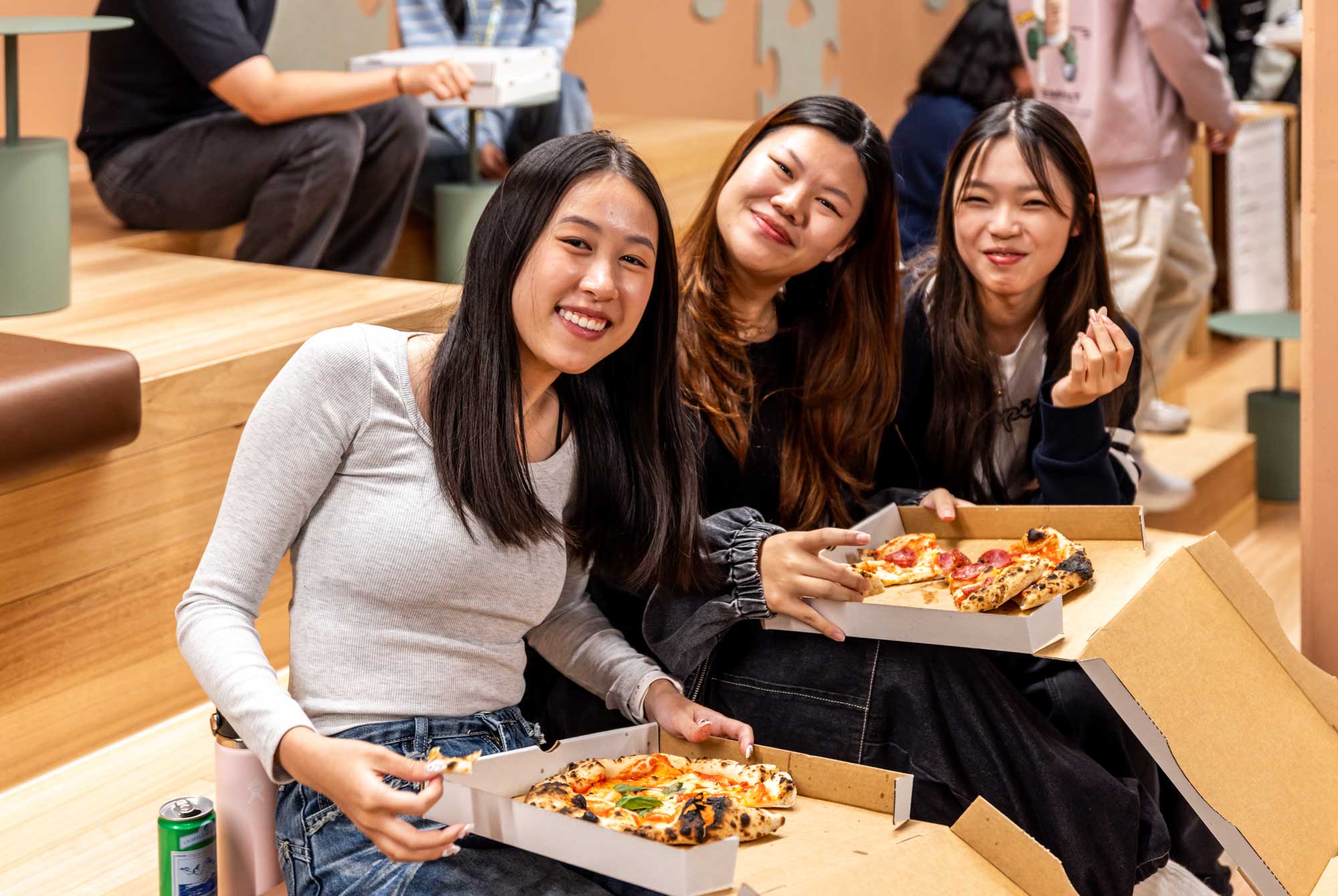 Three friends smiling with open pizza boxes.